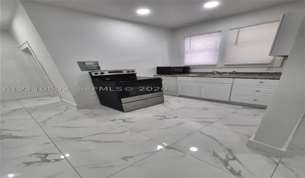 Kitchen featuring large-format veined tile flooring, white shaker-style cabinetry, high-contrast countertop, and stainless steel range