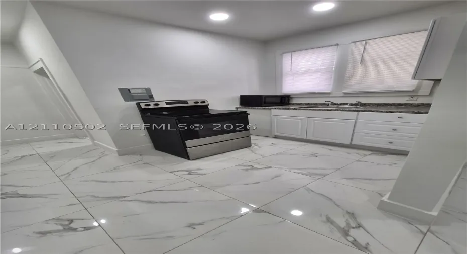 Kitchen featuring large-format veined tile flooring, white shaker-style cabinetry, high-contrast countertop, and stainless steel range