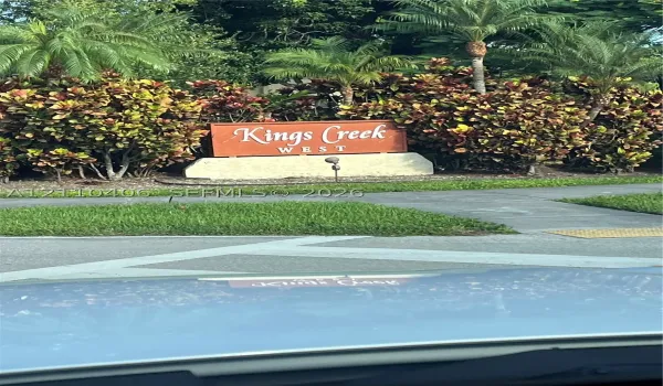 Community signage featuring structural masonry base and mature tropical landscaping including palm trees and croton shrubs