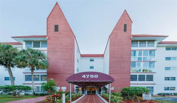 Multi-story exterior featuring a red brick facade, distinctive peaked roofline, a covered entrance canopy, and horizontal window rows