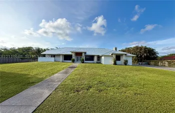 Single-story residence featuring a metal roof, stone-accented facade, expansive front lawn, and a concrete walkway