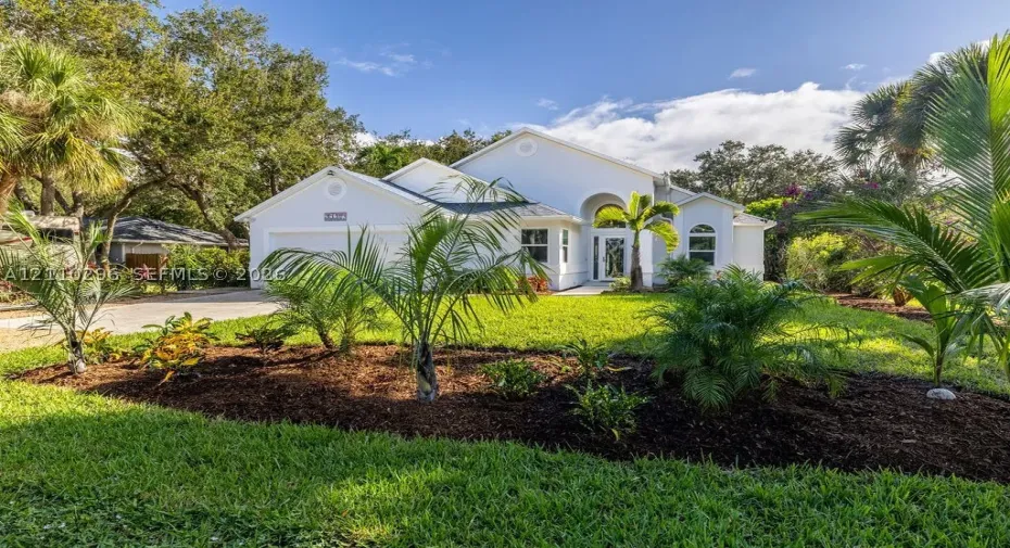 Stucco exterior residence featuring an arched entryway, gabled roofline, concrete driveway, and landscaped front yard with palm trees