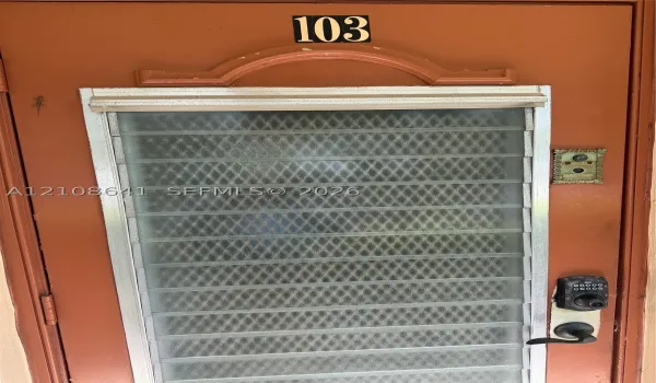 Solid entry door with a decorative arched transom, integrated metal security screen, push-button electronic keypad lock, and antique-style metal doorbell fixture