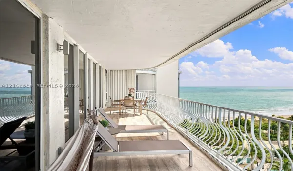 Expansive covered balcony featuring wood-finish flooring, full-length glass sliding doors, and decorative metal railings overlooking the ocean