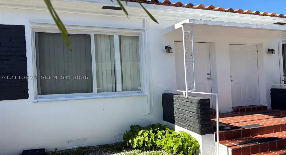 Exterior featuring white stucco finish, terracotta-style tiled entrance steps, clay tile roof accents, and black brick masonry detailing