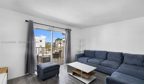 Living area featuring large-format tile flooring and sliding glass doors leading to a private balcony with metal railing