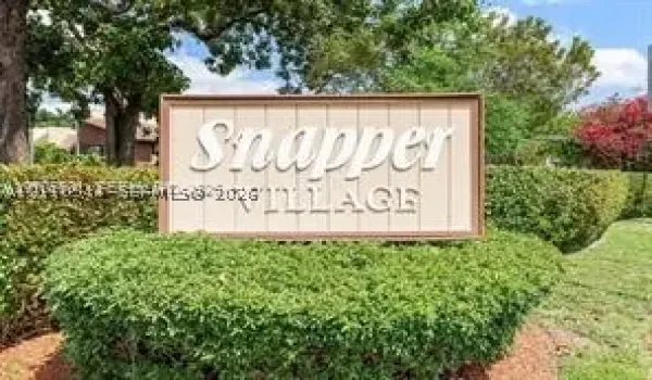 Community signage featuring a wood-frame monument with raised lettering, surrounded by manicured hedges and mature landscaping