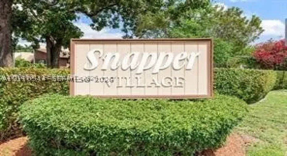 Community signage featuring a wood-frame monument with raised lettering, surrounded by manicured hedges and mature landscaping