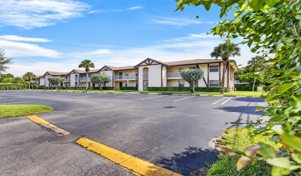 Two-story building featuring a neutral stucco exterior, brown trim, multi-gabled roofline, private balconies, and dedicated asphalt parking