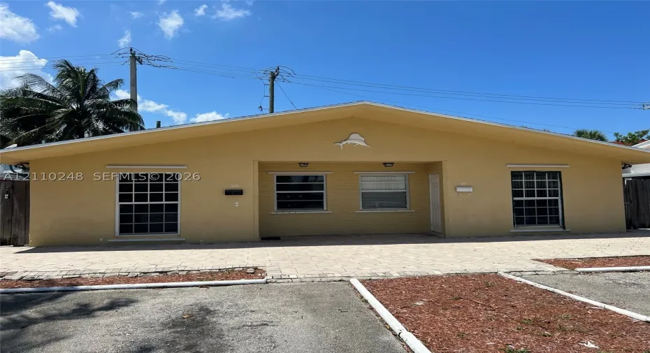 Single-story exterior featuring a stucco facade, gable roofline, paved brick driveway, and multi-pane windows