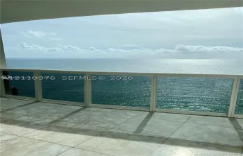 Covered balcony featuring large-format tile flooring and a glass-paneled railing overlooking the ocean