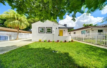 Single-story exterior featuring a light-toned stucco facade, a vibrant front entry door, a covered porch, and perimeter white metal fencing