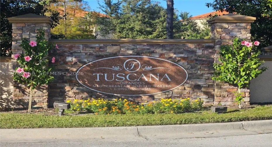 Stone-veneer community monument featuring pillars with capstones, embedded oval signage, and professionally landscaped flower beds