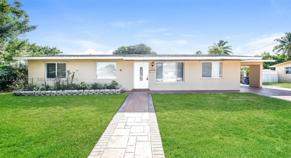 Single-story exterior featuring a concrete-tile walkway, stone-block landscaping border, and covered carport