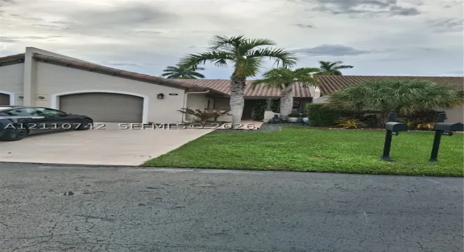 Stucco exterior featuring a concrete tile roof, an arched garage entrance, and a paved driveway