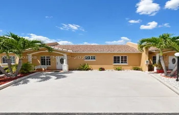 Stucco exterior featuring a clay tile roof, arched entryway with decorative columns, and a concrete driveway