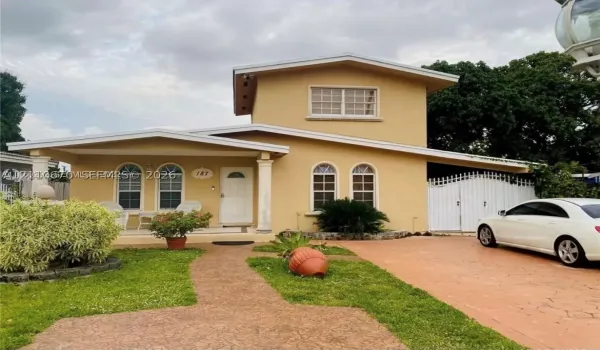 Two-story exterior featuring a covered front porch, arched window detailing, paved driveway, and decorative gate
