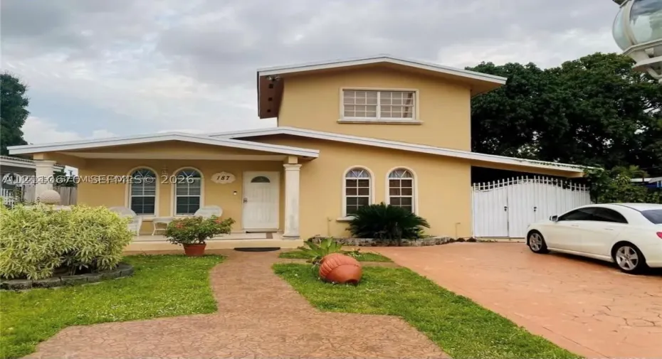 Two-story exterior featuring a covered front porch, arched window detailing, paved driveway, and decorative gate