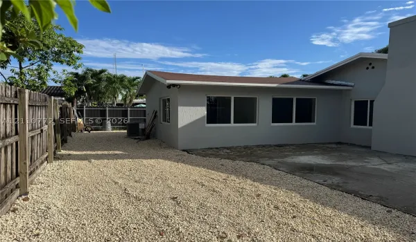 Exterior view featuring a neutral-toned stucco finish, low-maintenance gravel ground cover, and enclosed wooden perimeter fencing