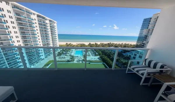 Private balcony featuring a glass-panel railing and open-air access to coastal scenery, a swimming pool, and groomed grounds