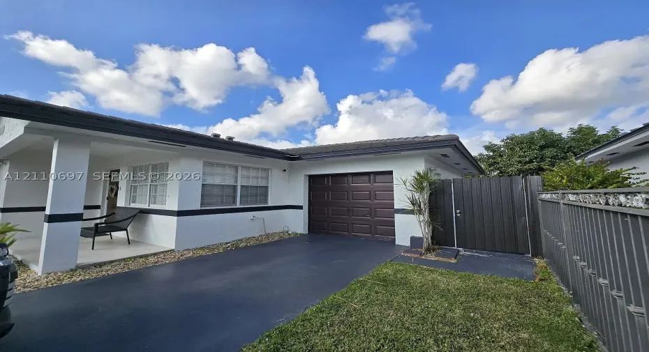 Single-story exterior featuring a covered front porch, dark-toned sectional garage door, paved driveway, and metal privacy fencing