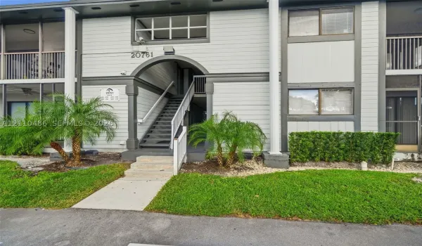Multi-story exterior featuring lap siding, arched entryway, staircase with metal railing, private balconies, and landscaped grounds