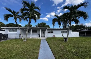 Single-story exterior featuring a covered entryway with decorative columns, a concrete walkway, and mature palm trees