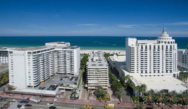 Aerial perspective of high-rise structures situated along the coastline, featuring beachfront access, multiple tiered balconies, and paved surface parking