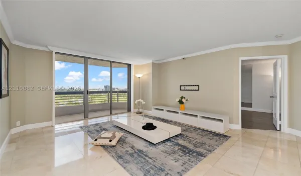 Living area featuring neutral stone flooring, crown molding, and floor-to-ceiling sliding glass doors opening to a private balcony