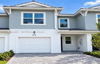 Stucco facade featuring gabled roofline, decorative eave brackets, paver driveway, and single-car garage