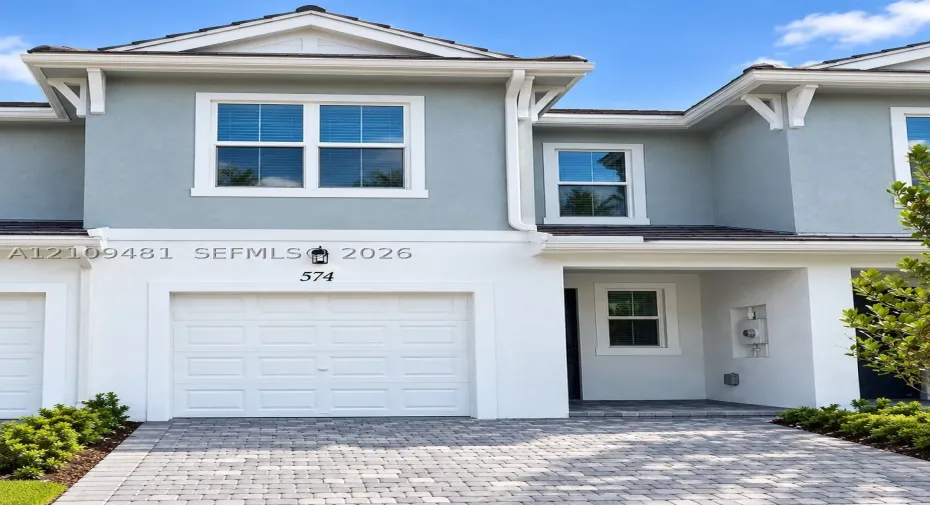 Stucco facade featuring gabled roofline, decorative eave brackets, paver driveway, and single-car garage