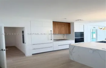 Kitchen featuring a stone-surface island, built-in integrated refrigerator, wall-mounted double oven, custom flat-panel cabinetry with wood-finish upper accents, and light-toned wood-finish flooring