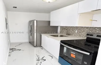 Kitchen featuring white gloss cabinetry, stone-finish countertops, stainless steel refrigerator, black finish range, and herringbone tile backsplash over marble-finish flooring