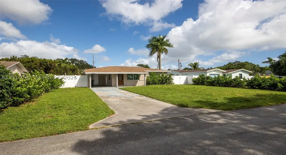 Single-story exterior featuring a hip roof, covered front entryway, concrete driveway, and white vinyl privacy fencing