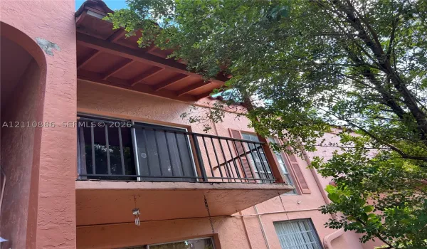 Stucco exterior featuring a second-story balcony with a metal railing, exposed beam ceiling, and shutter-framed windows