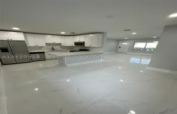Kitchen featuring white shaker-style cabinetry, quartz countertops, a peninsula with bar seating, stainless steel appliances, and large-format porcelain tile flooring