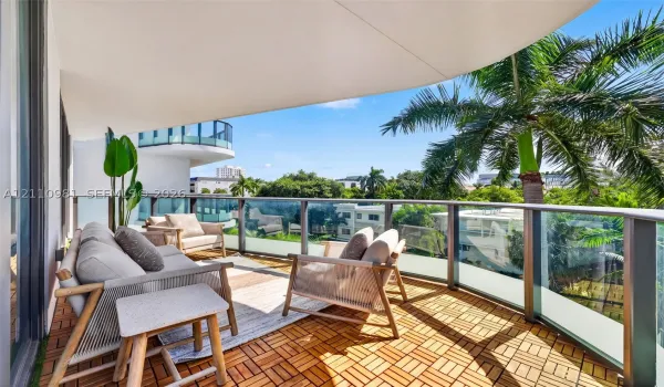 Covered balcony featuring wood-finish deck tiling, glass-paneled railings, and a curved architectural overhang