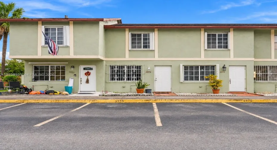 Multi-unit exterior featuring two-story stucco facade, exterior window security bars, grid-pattern windows, and dedicated asphalt parking