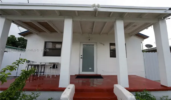 Covered front porch featuring structural columns, a painted concrete floor, exposed wood ceiling rafters, and an exterior door with a frosted glass panel