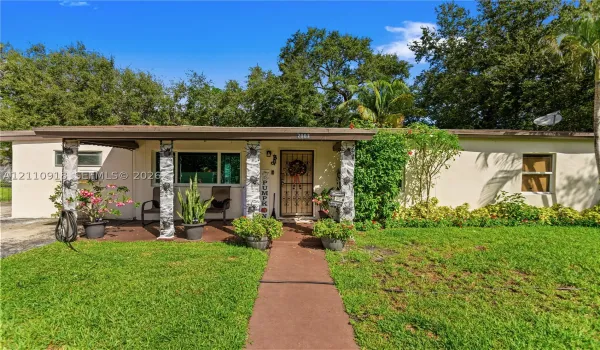 Single-story exterior featuring a concrete walkway, covered front porch, textured masonry support columns, and metal security door
