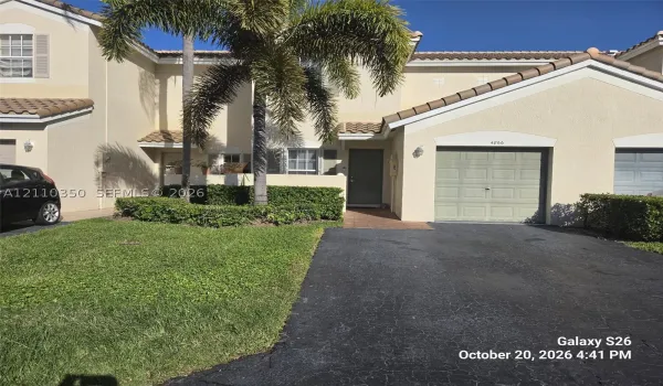 Stucco exterior featuring a tiled roof, attached single-car garage, paved driveway, and mature landscaping