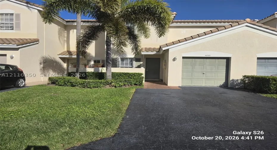 Stucco exterior featuring a tiled roof, attached single-car garage, paved driveway, and mature landscaping