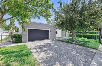 Detached garage with large-format stone-textured exterior cladding, paved brick driveway, metal gate, and manicured landscaping