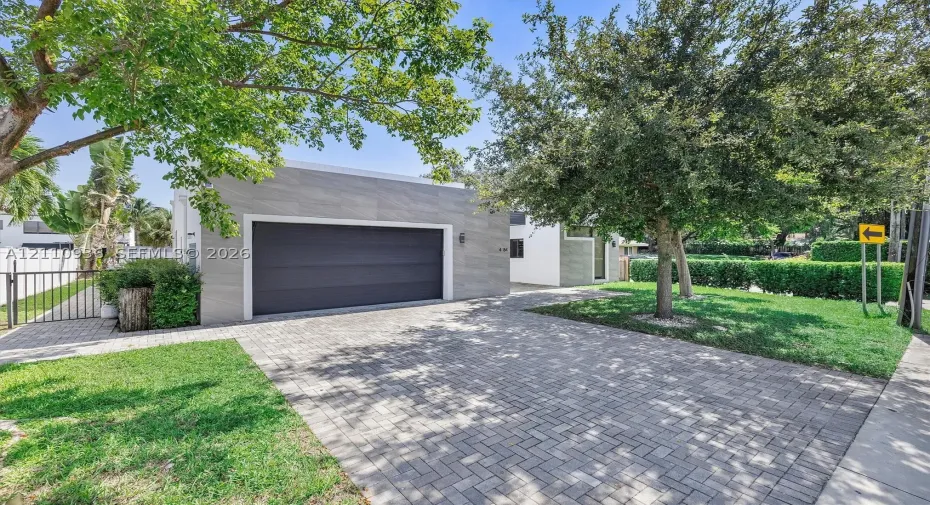 Detached garage with large-format stone-textured exterior cladding, paved brick driveway, metal gate, and manicured landscaping