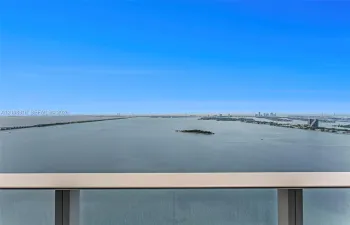 Elevated balcony featuring a glass panel railing with a metallic frame and expansive water and distant skyline scenery