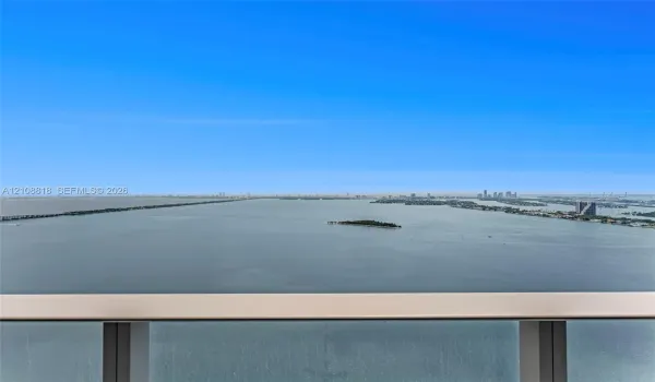 Elevated balcony featuring a glass panel railing with a metallic frame and expansive water and distant skyline scenery