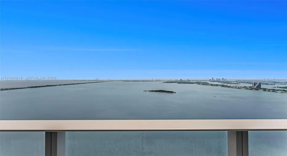 Elevated balcony featuring a glass panel railing with a metallic frame and expansive water and distant skyline scenery