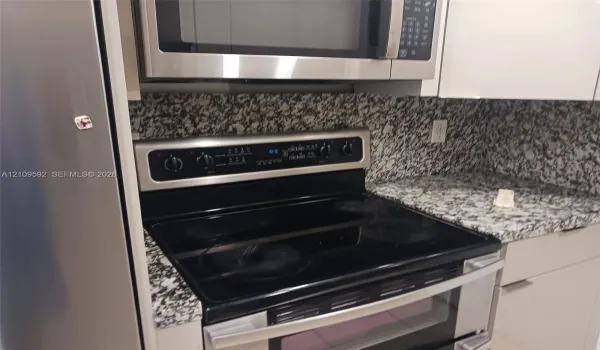 Kitchen featuring stainless steel appliances, a glass-top electric range, a built-in microwave, stone-finish countertops, and white cabinetry