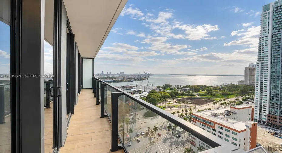 Covered balcony featuring wood-finish tile flooring, sleek black metal railings, and integrated glass panels