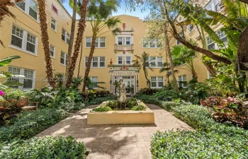 Stucco exterior featuring decorative masonry accents, a central courtyard fountain, multi-pane windows, and paved walkways surrounded by lush mature landscaping